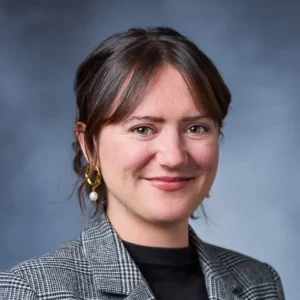 Emma Tucher wearing black shirt, under black plaid jacket and white drop earrings.