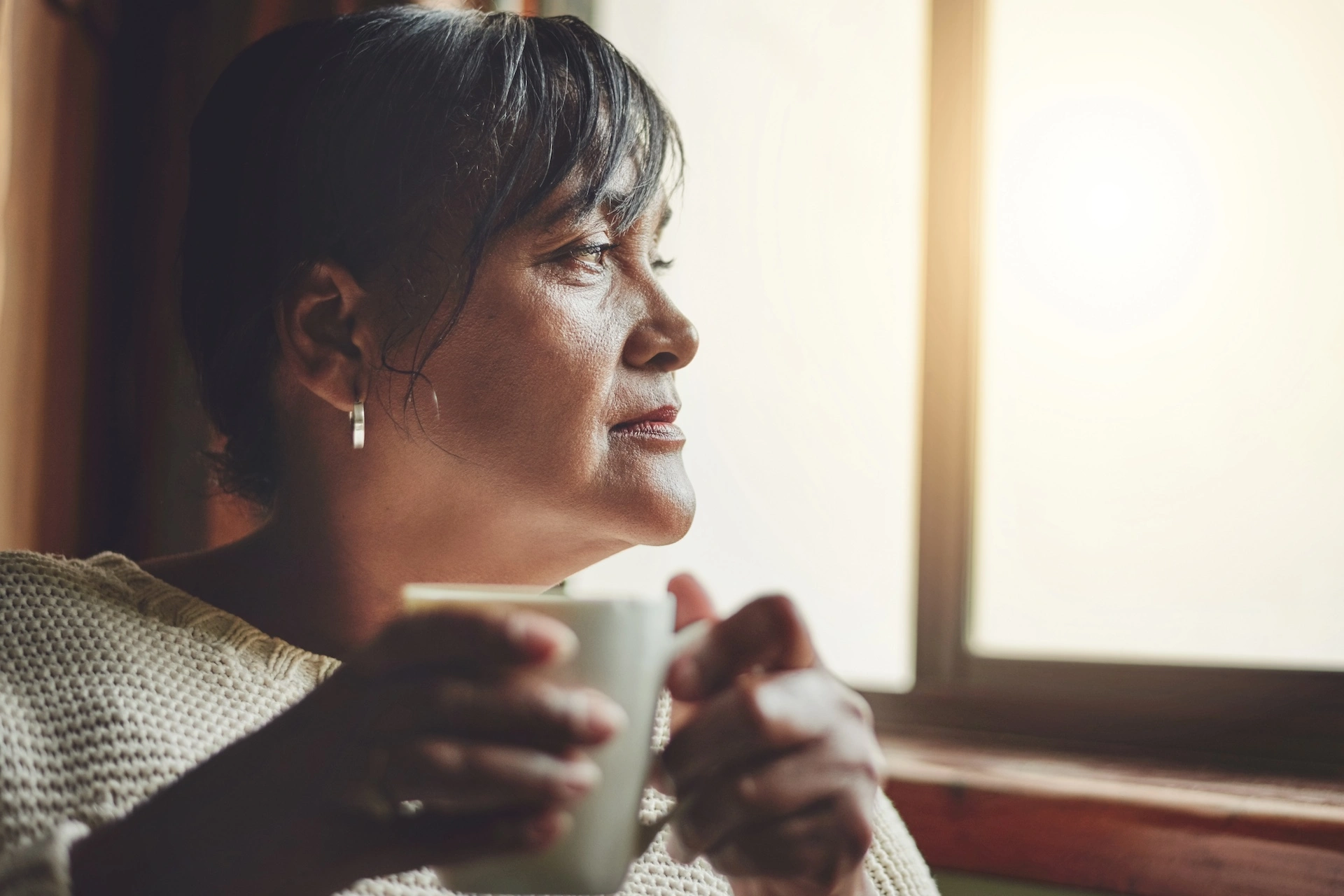 Woman with dark hair holding coffee mug looking out window