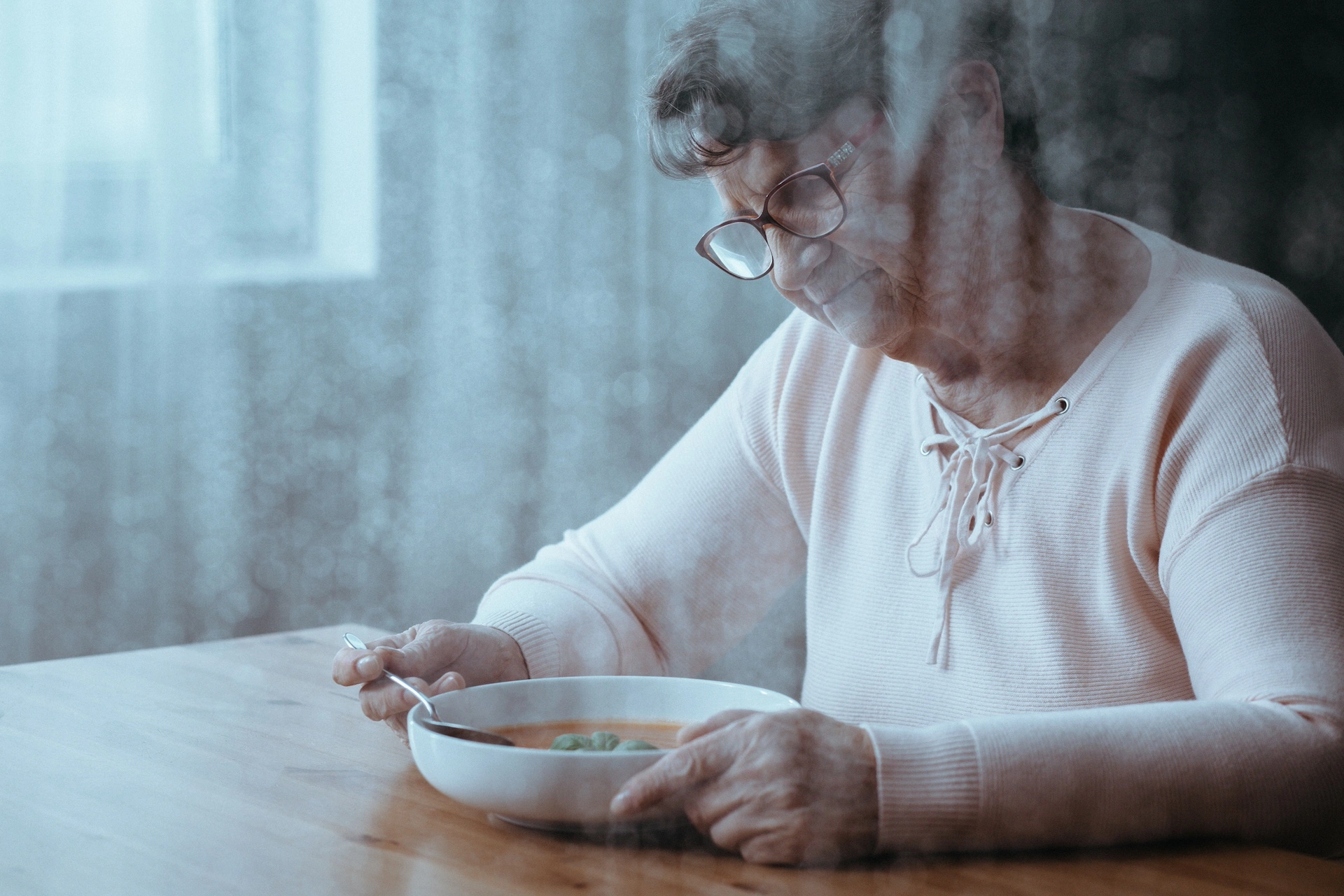 lonely older woman wearing glasses and a sweater eating a bowl of soup