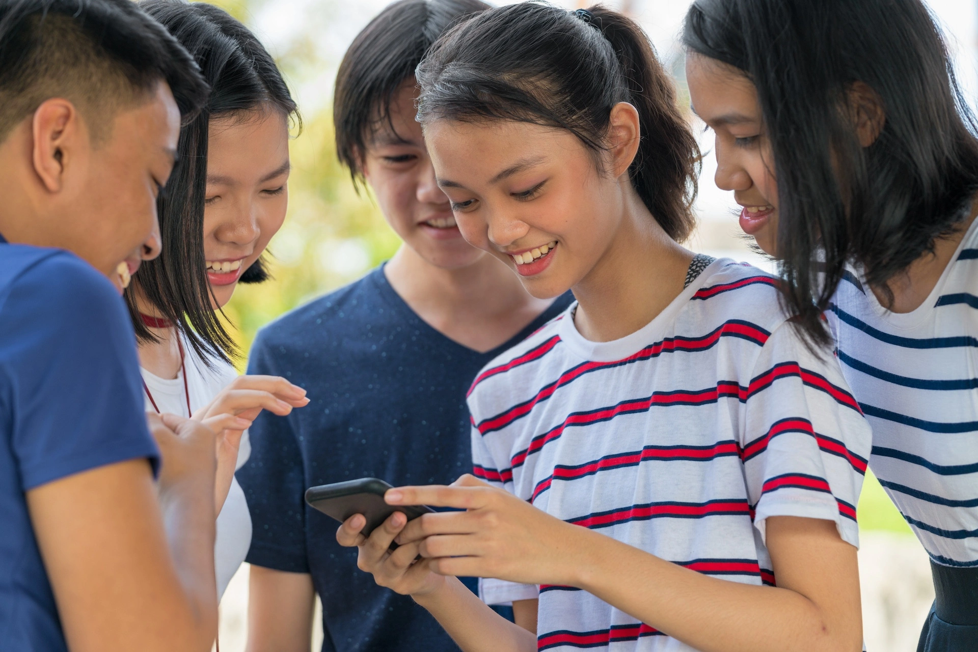 five asian girls and boys looking at a phone one girl is holding