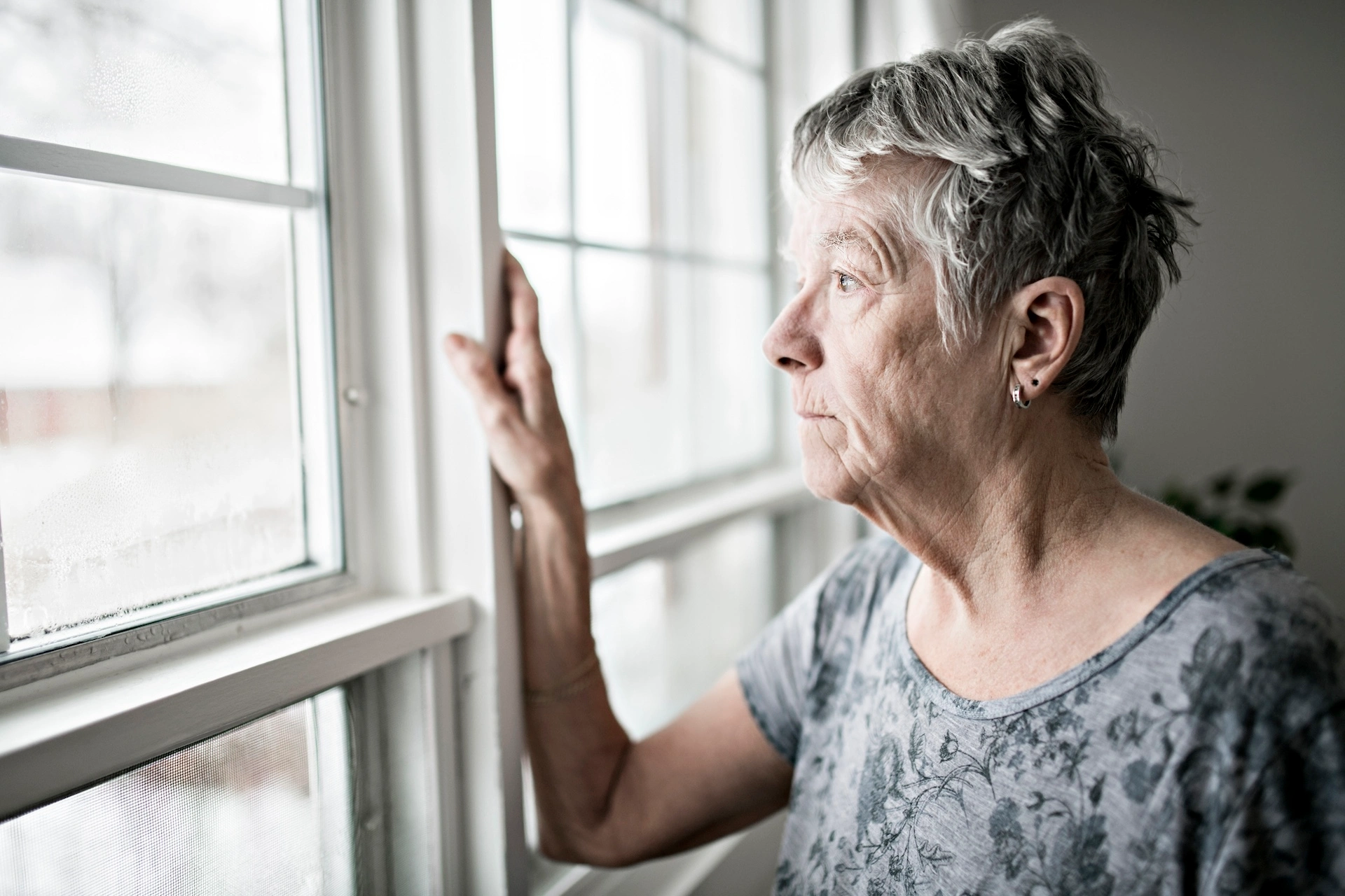 Older gray-haired woman staring out window.